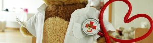 Ein rotes, herzförmiges Stethoskop mit einem Button, darauf ein Teddybär mit der Aufschrift „Teddybärkrankenhaus Rosenheim“.