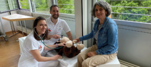 Andrea Janshen sitzt neben dem kranken Kuschelttier und hölt dessen Hand, während es von den beiden Teddydocs untersucht wird.