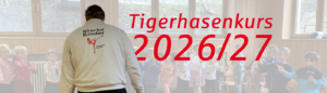 Headergrafik für einen „Tigerhasenkurs 2026/27“: In einem hellen Raum steht ein Trainer mit dem Rücken zur Kamera vor einer Gruppe von Kindern. Auf seiner Jacke steht „Starke Kinder“ mit einem Motiv aus dem Kampfsport. Im Vordergrund ist groß und rot der Schriftzug „Tigerhasenkurs 2026/27“ zu sehen.